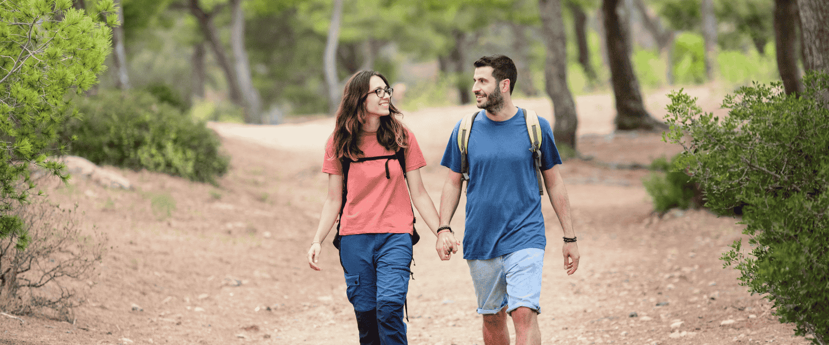 A young couple in their 30s hiking on a trail with backpacks.