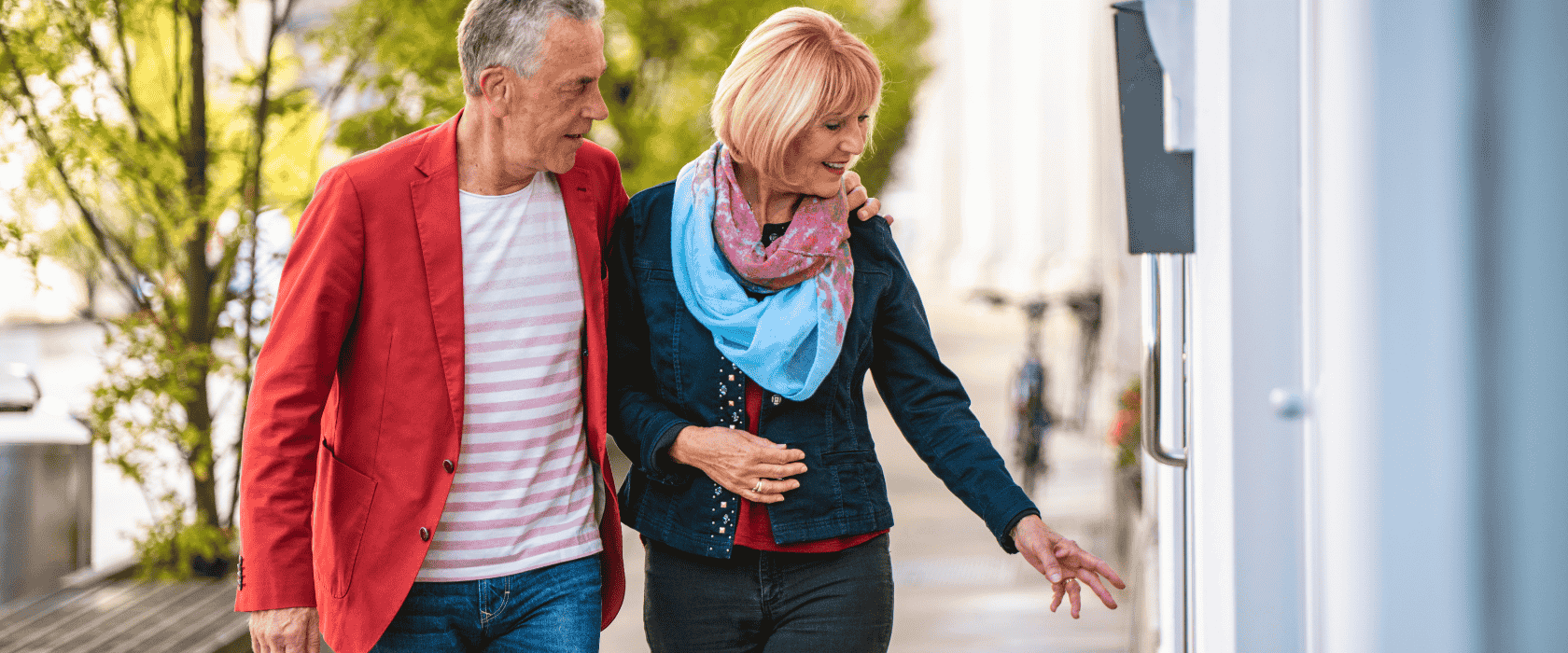A couple in their 60s walking down a sidewalk looking in the business windows.