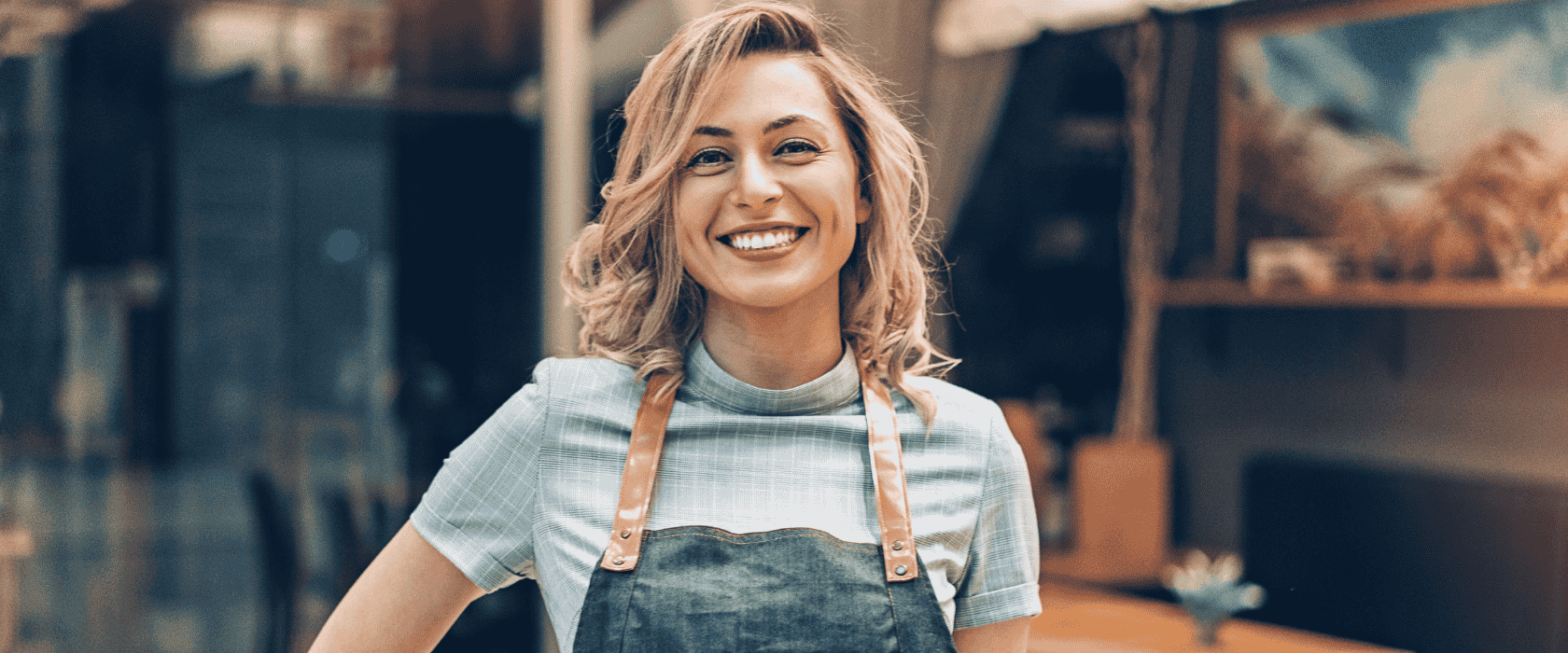 A young female business owner in an apron smiling at the camera.