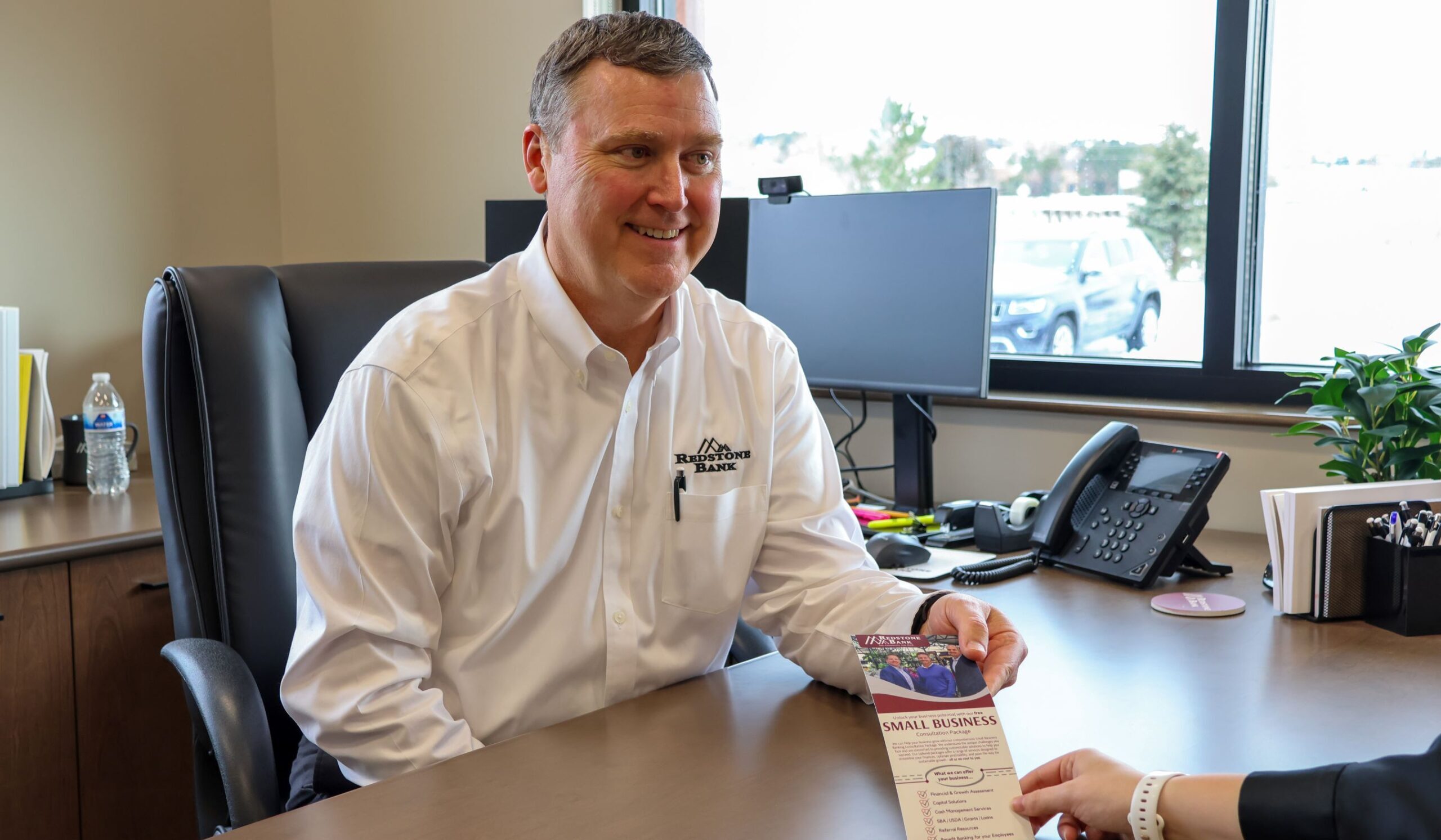 Jason Whyte, treasury management officer at Redstone sitting at his desk handing a brochure to a client